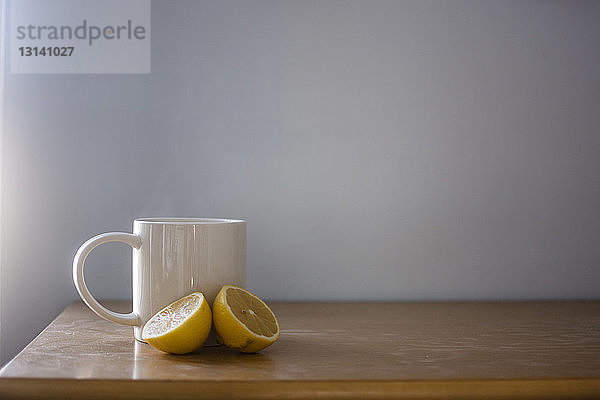Geschnittene Zitrone mit Tee auf Holztisch vor weißer Wand