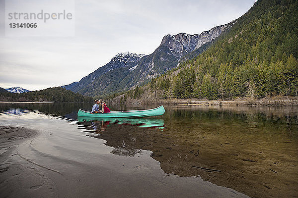 Junges Paar sitzt im Kanu auf dem See vor Bergen
