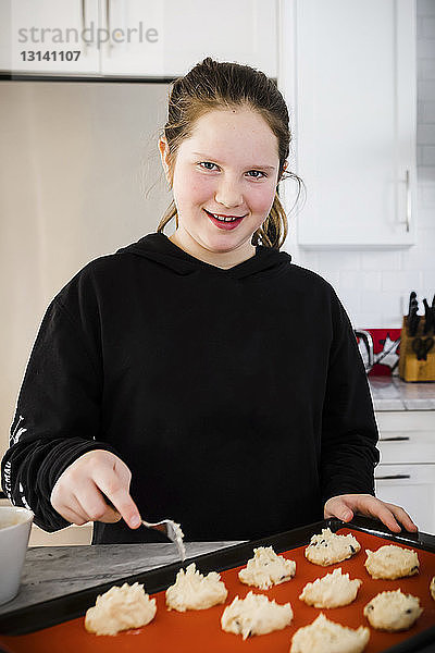 Porträt eines Mädchens  das zu Hause in der Küche Teig auf ein Backblech legt