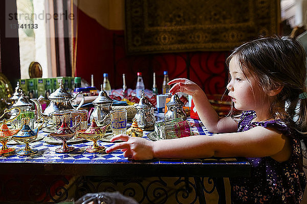 Seitenansicht eines Mädchens mit Zauberlampen und Teekannen auf dem Tisch zu Hause