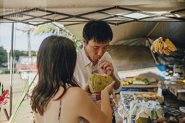 Ehepaar trinkt Kokosnusswasser am Marktstand