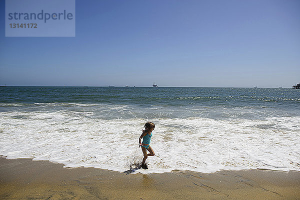 Verspieltes Mädchen rennt am Strand von Seal Beach gegen den klaren Himmel auf Surfbrettern