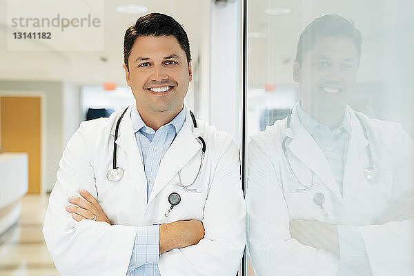 Porträt eines selbstbewussten Arztes mit verschränkten Armen im Krankenhauskorridor stehend