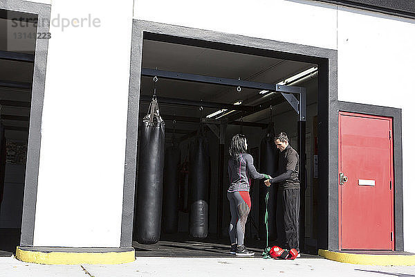 Männlicher Trainer  der die Hand einer Athletin mit Armband im Fitnessstudio umwickelt