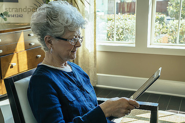 Ältere Frau benutzt Tablet-Computer  während sie sich zu Hause auf einem Stuhl entspannt
