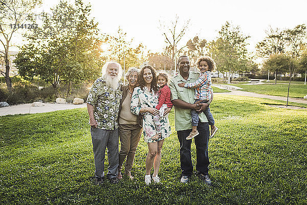 Porträt einer glücklichen Mehrgenerationen-Familie auf einem Grasfeld im Park