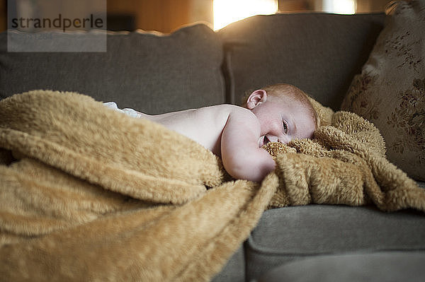 Kleiner Junge liegt zu Hause auf dem Sofa