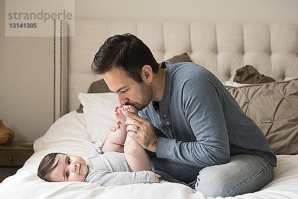 Vater küsst dem Sohn die Füße  während er zu Hause im Bett sitzt