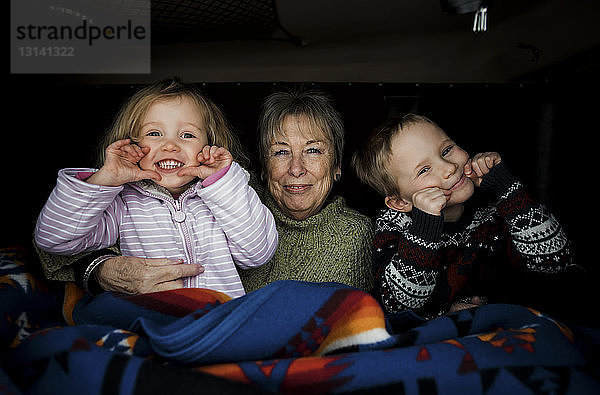 Porträt von lächelnden Enkelkindern mit Großmutter  die im Dachzelt auf dem Auto sitzen