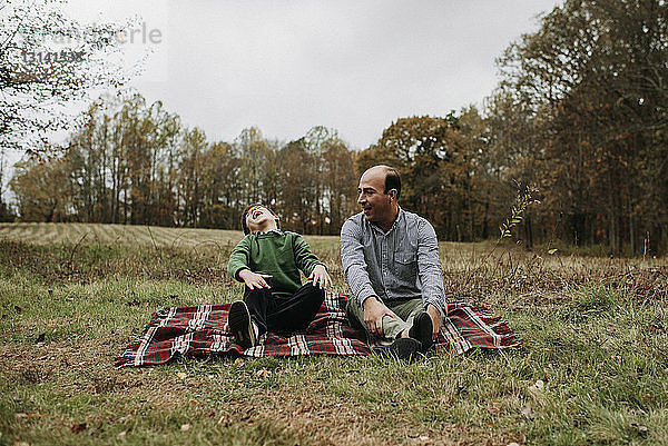 Glücklicher Vater mit Sohn sitzt im Park auf einer Decke gegen den Himmel