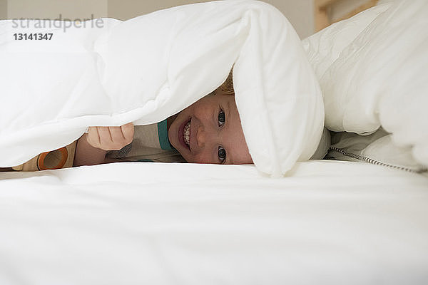 Porträt eines lächelnden Mädchens in Bettdecke auf Bett