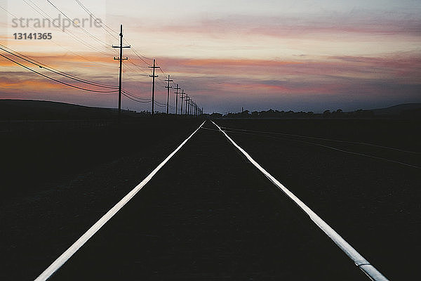 Eisenbahnschienen auf Silhouettenlandschaft vor bewölktem Himmel bei Sonnenuntergang