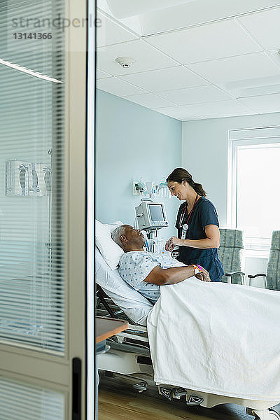 Krankenschwester betrachtet schlafende ältere Patientin  die auf einem Bett auf der Krankenhausstation liegt  durch die Tür