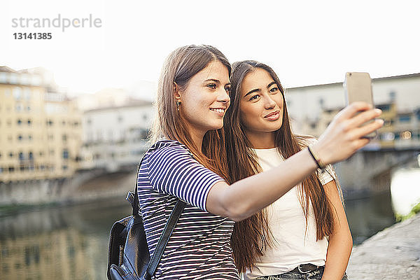 Lächelnde Freunde nehmen sich mit Smartphone gegen Kanal in der Stadt