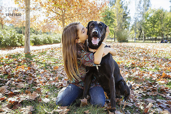 Mädchen küsst schwarzen Hund  während sie im Herbst im Park sitzt