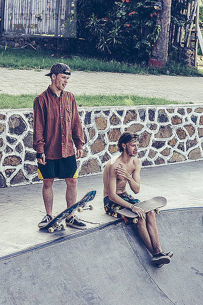 Junge männliche Freunde ruhen sich mit Skateboards am Rand eines Betonpools aus