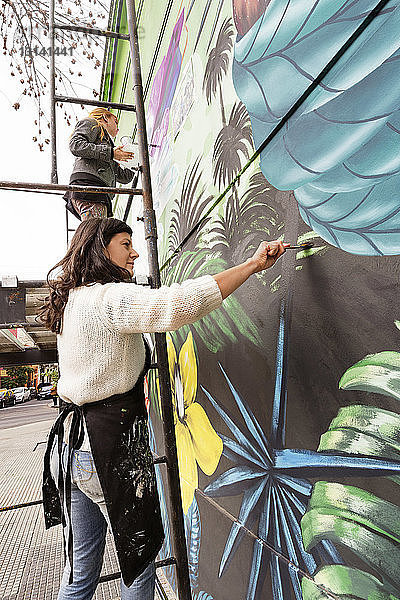 Konzentrierte Künstlerinnen malen Wandbilder an der Wand
