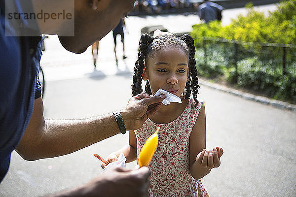 Vater reinigt Gesicht der Tochter mit Gewebe im Park
