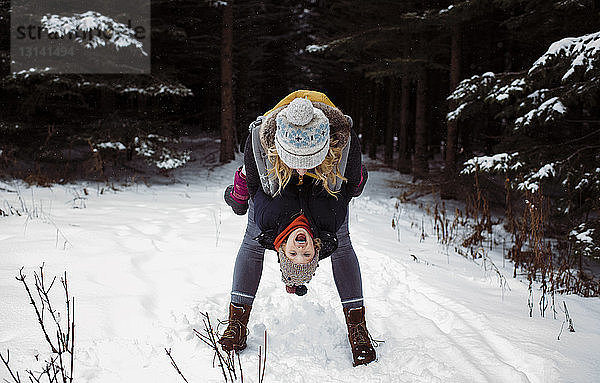 Fröhliche Mutter spielt mit ihrer Tochter  während sie im Winter im Wald steht