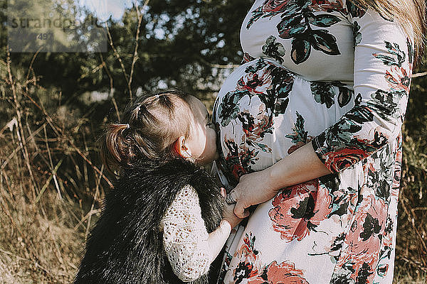 Liebende Tochter küsst den Bauch der schwangeren Mutter  während sie im Wald steht