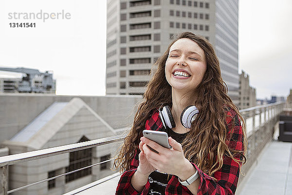 Fröhliche Frau benutzt Smartphone  während sie im Terrassencafé steht