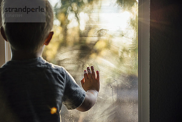 Rückansicht eines Jungen  der zu Hause durch ein Fenster schaut