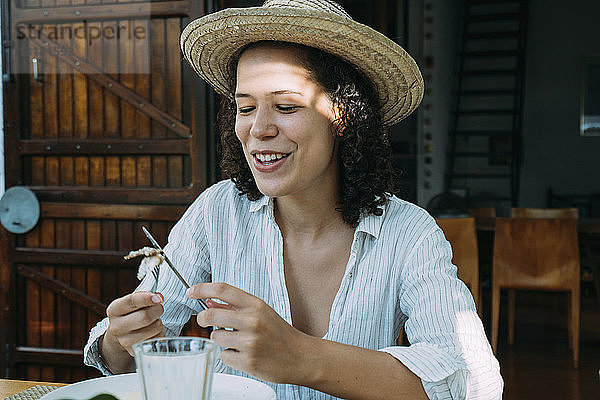 Lächelnde Frau isst Essen  während sie in einer Hütte sitzt