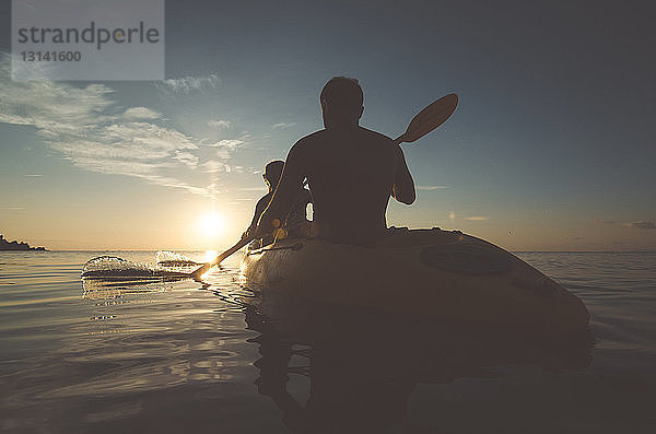 Scherenschnitt-Freunde beim Kajakfahren auf dem Meer bei Sonnenuntergang