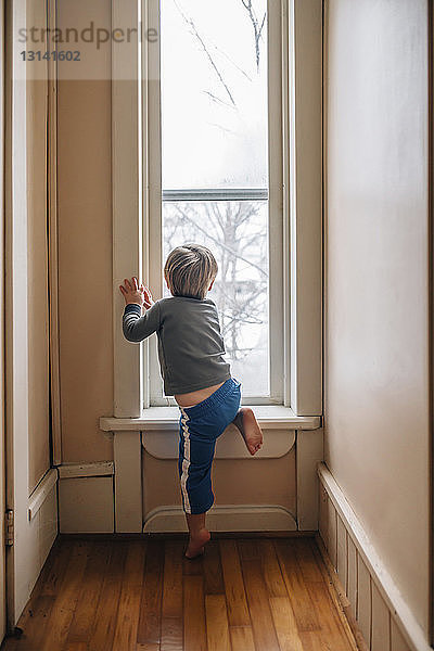 Rückansicht eines neugierigen Jungen  der durch ein Fenster schaut