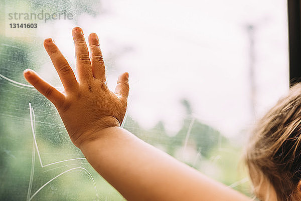 Beschnittenes Bild eines Mädchens  das zu Hause Fensterglas berührt