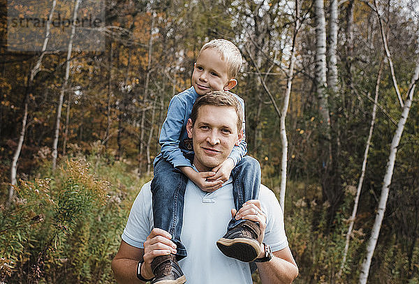Porträt eines Vaters  der seinen Sohn auf den Schultern trägt  während er im Wald steht