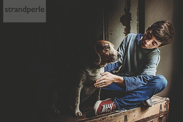 Teenager mit Hund sitzt auf Holzkiste in der Dunkelkammer zu Hause