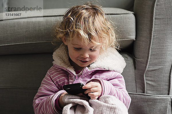 Mädchen benutzt Mobiltelefon  während sie zu Hause am Sessel sitzt