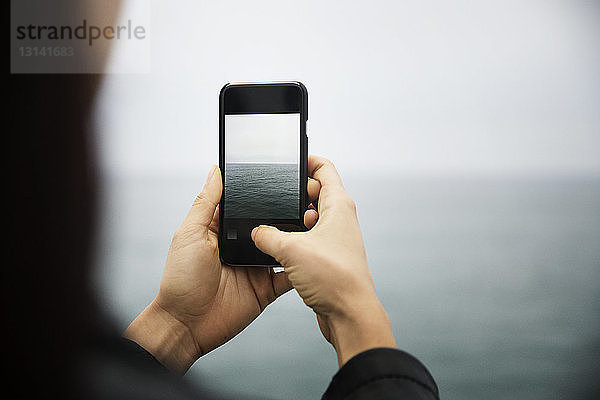 Ausschnitt einer Frau  die mit ihrem Mobiltelefon das Meer fotografiert