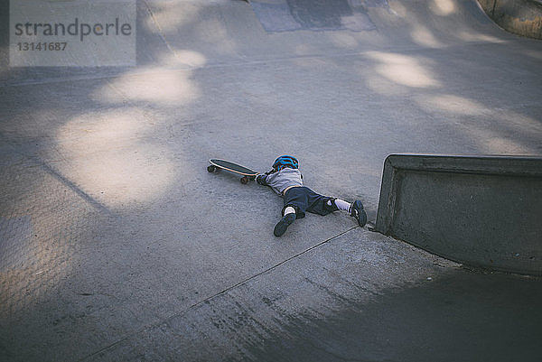 Hochwinkelaufnahme eines Jungen  der im Park vom Skateboard fällt