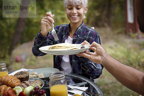 Ausgeschnittenes Bild eines Mannes  der einer jungen Frau während des Frühstücks Pfannkuchen anbietet