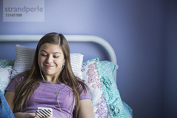 Lächelndes Mädchen benutzt Smartphone beim Entspannen im Bett