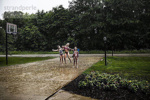 Verspielte Schwestern in voller Länge  die während der Regenfälle auf dem Fußweg im Park tanzen