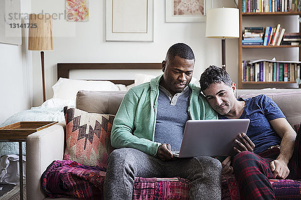 Multi-ethnische homosexuelle Männer mit Laptop auf dem Sofa zu Hause