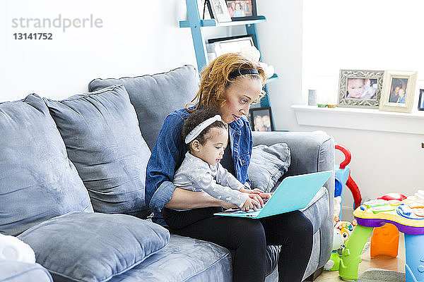 Mutter und Tochter benutzen einen Laptop-Computer  während sie auf dem Sofa sitzen