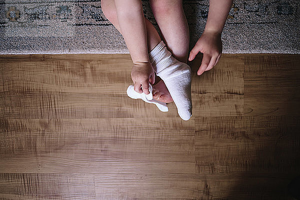 Draufsicht eines Mädchens  das zu Hause auf dem Teppich sitzend seine Socken auszieht