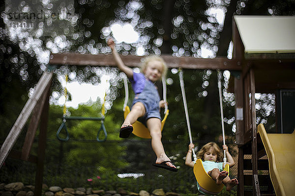 Niedriger Blickwinkel auf Schwestern  die auf dem Spielplatz schaukeln