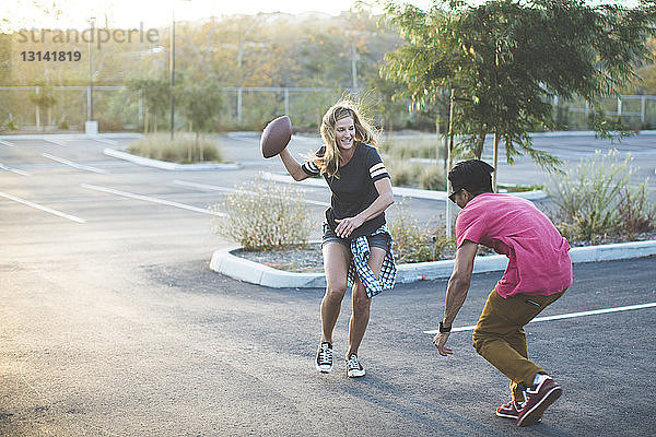 Glückliche Freunde spielen mit American Football auf dem Parkplatz