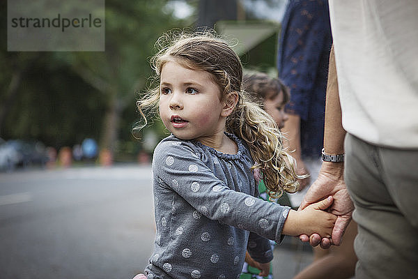Mädchen schaut weg  während sie die Hand des Vaters auf der Straße hält