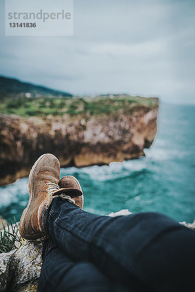 Niedriger Teil eines Mannes sitzt auf einem Berg am Meer vor bewölktem Himmel