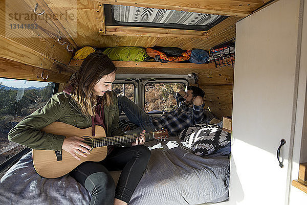 Frau spielt Gitarre  während sie mit einem Freund im Wohnmobil sitzt