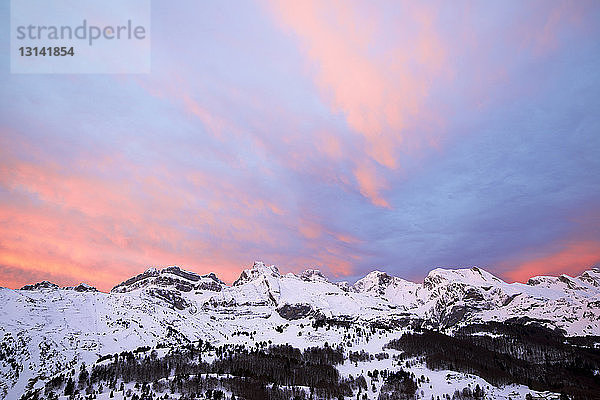 Tiefwinkel-Szenenansicht von schneebedeckten Bergen vor dramatischem Himmel bei Sonnenuntergang