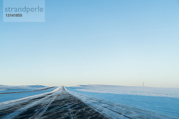 Landschaftliche Ansicht der Straße inmitten einer schneebedeckten Landschaft vor klarem Himmel