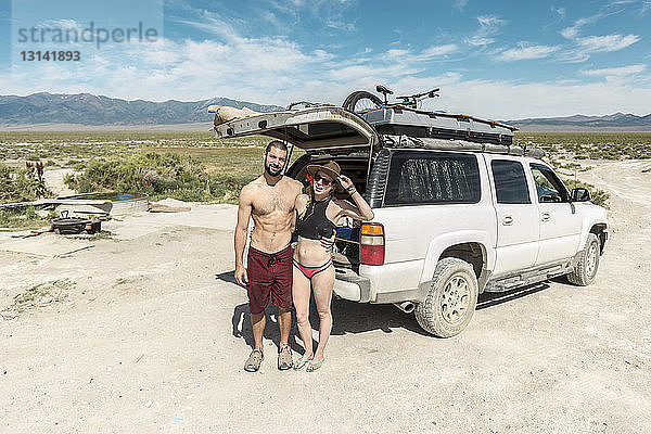 Hochwinkel-Porträt eines Paares in Badebekleidung  das an einem sonnigen Tag in Spencer Hot Springs gegen ein Geländefahrzeug steht