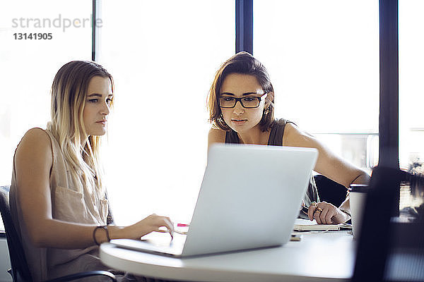 Geschäftsfrauen benutzen Laptop  während sie im Kreativbüro sitzen